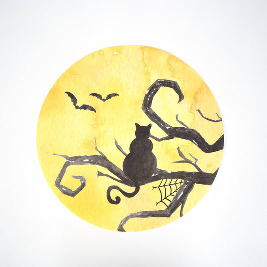 Placemats with a Halloween-themed design with a black cat on a branch, bats, and spider web against a yellow moonlit sky.
