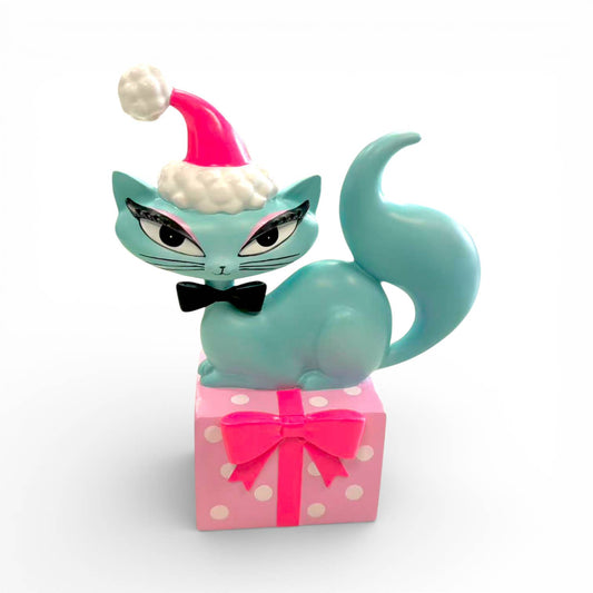 Cat figurine with a Santa hat on a pink gift box with white polka dots.