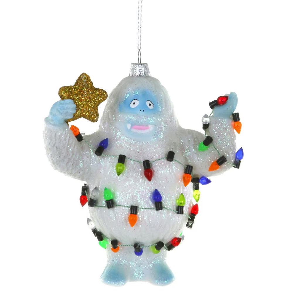 A white glittery yeti Christmas ornament holding a gold glitter star, wrapped in multicolored holiday lights.