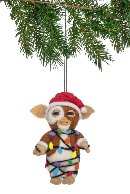A felt Christmas ornament made to resemble Gizmo. Wearing a red Santa hat and wrapped in multicolored holiday lights