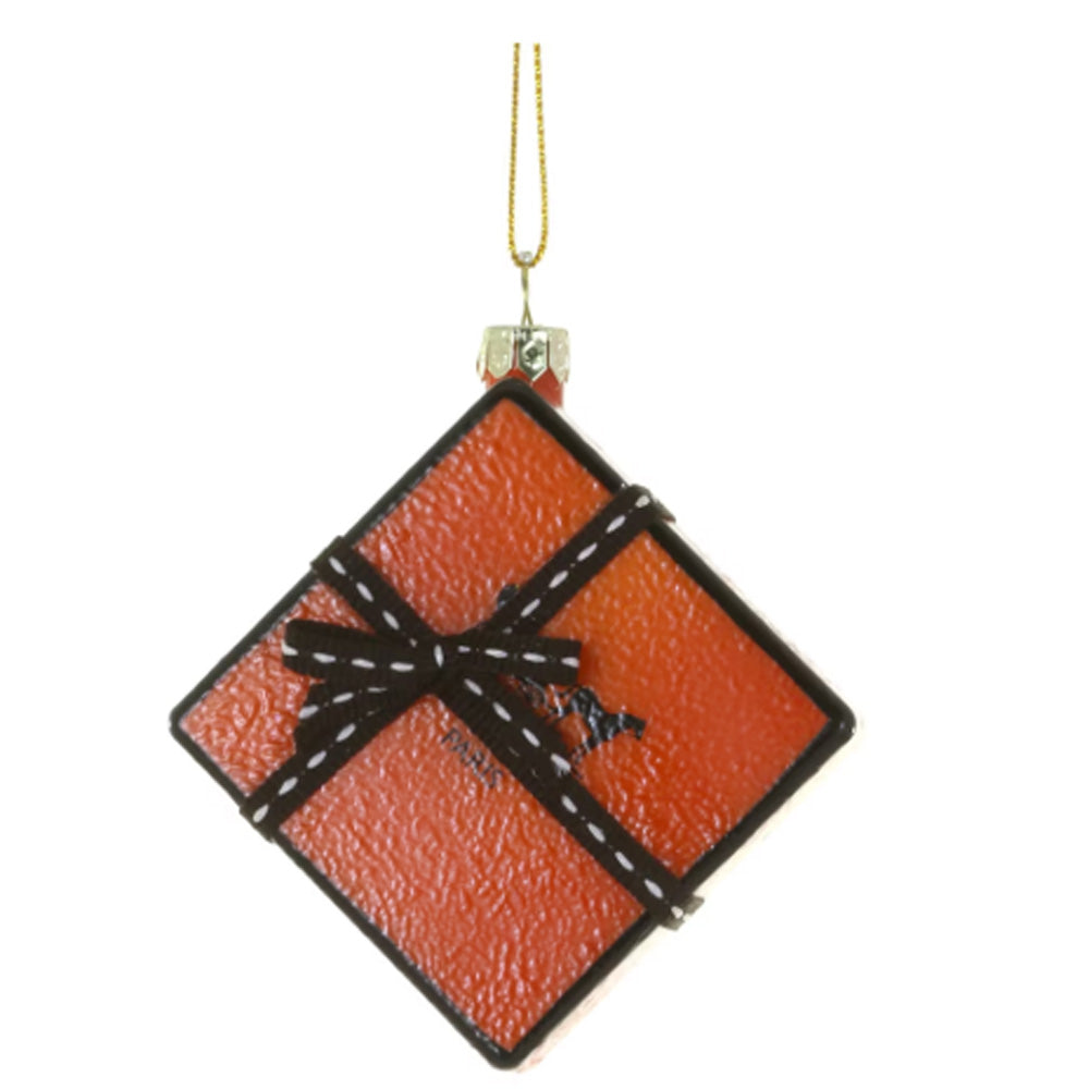 An orange gift box Christmas ornament with a black ribbon and white dashed bow details, hanging from a gold string.