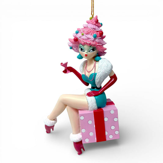 Decorative hanging ornament of a glamourous female character with pink hair and a blue dress, sitting on a gift box.