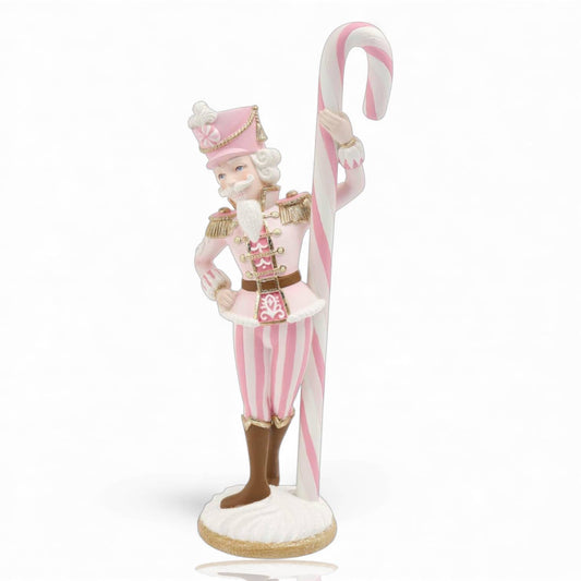 Decorative figurine of a nutcracker in pink and white attire holding a candy cane .
