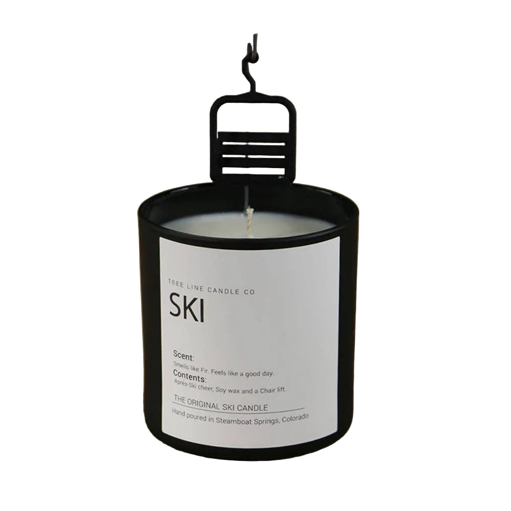 A black glass jar candle with a white label reading 'SKI'. A black metal ski chair hangs over the candle wick.  