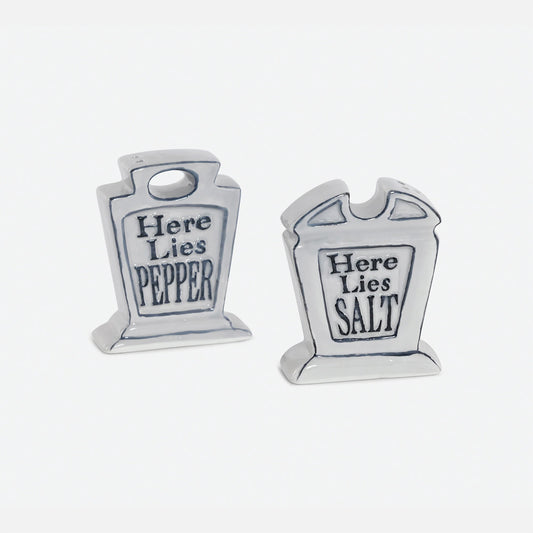 A pair of small tombstone-shaped salt and pepper shakers. One reads 'Here Lies PEPPER' and the other reads 'Here Lies SALT' in dark lettering.