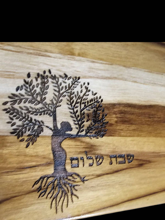 Wooden cutting board with a tree of life engraving and woman. Hebrew text reads Shabbat shalom.
